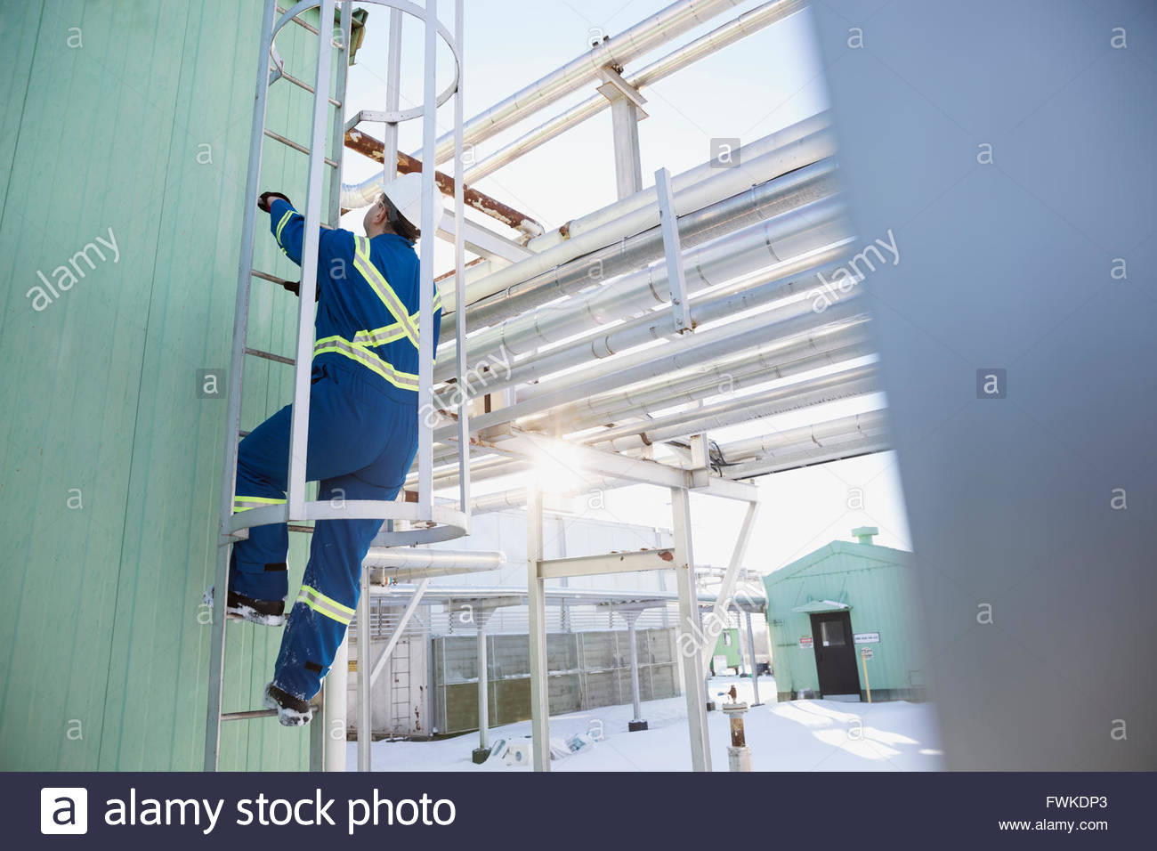 Lavoratore di sesso maschile di arrampicata impianto gas serbatoio di stoccaggio scaletta Foto Stock