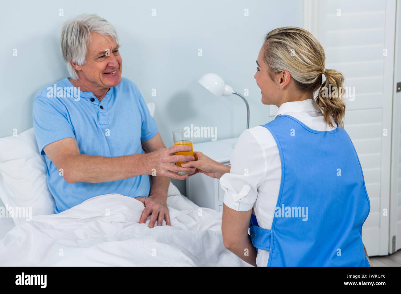 L'infermiera dando succo sorridente uomo senior Foto Stock