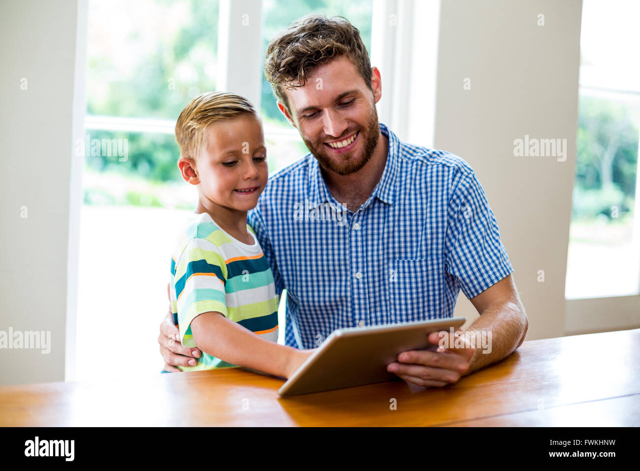 Padre e figlio cercando in tavoletta digitale in casa Foto Stock