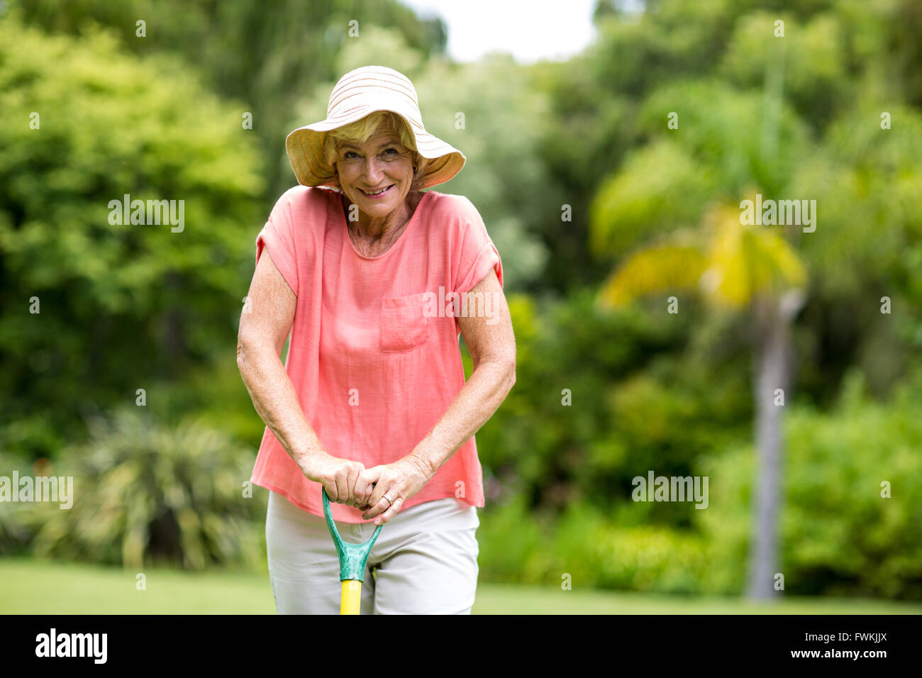 Senior woman in hat in piedi con rastrello in cantiere Foto Stock