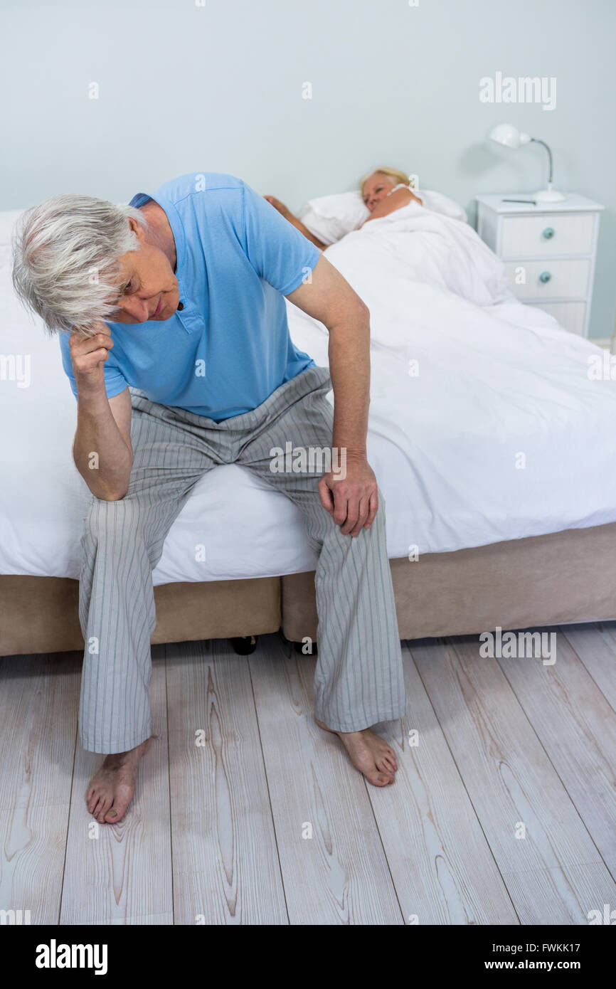 Tensionata senior uomo tocca la testata durante la donna che dorme sul letto Foto Stock