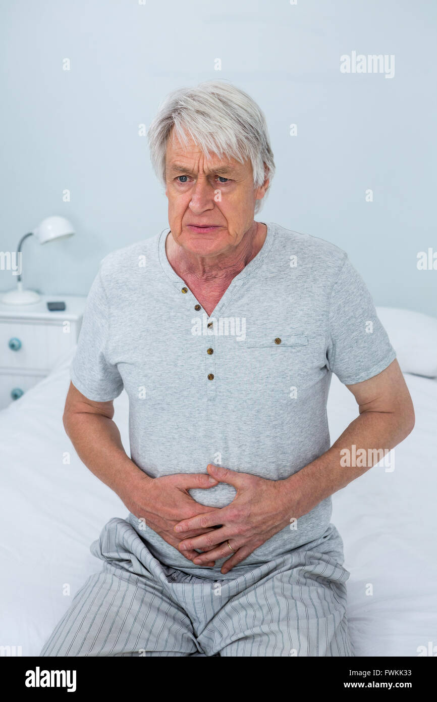Senior uomo toccando lo stomaco mentre è seduto sul letto Foto Stock