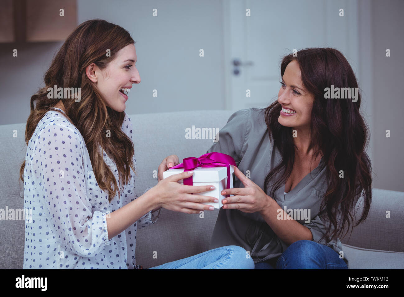 Donna dando un presente al suo amico in salotto Foto Stock