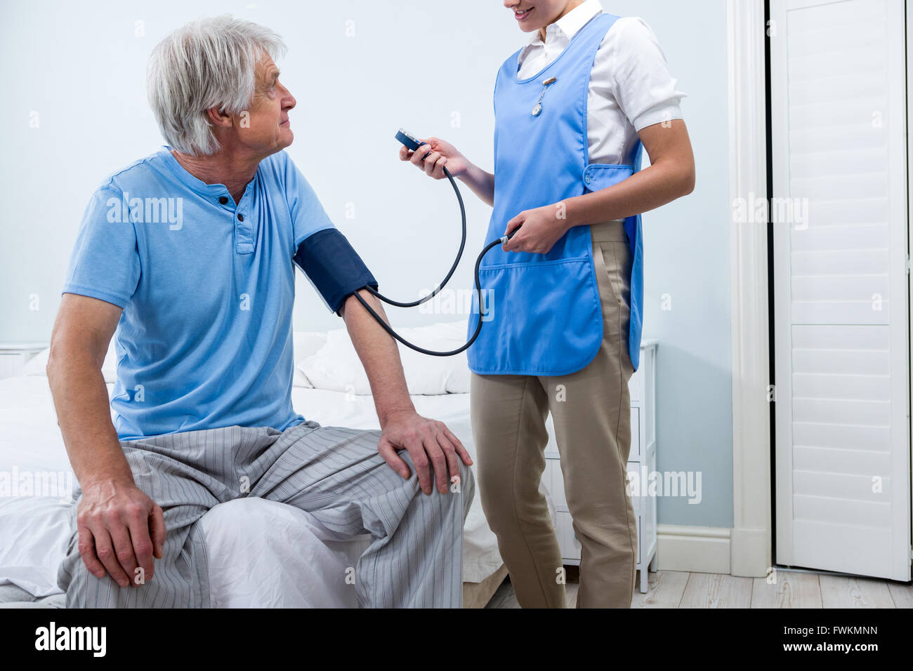 L'infermiera controllando la pressione del sangue di uomo senior a casa Foto Stock
