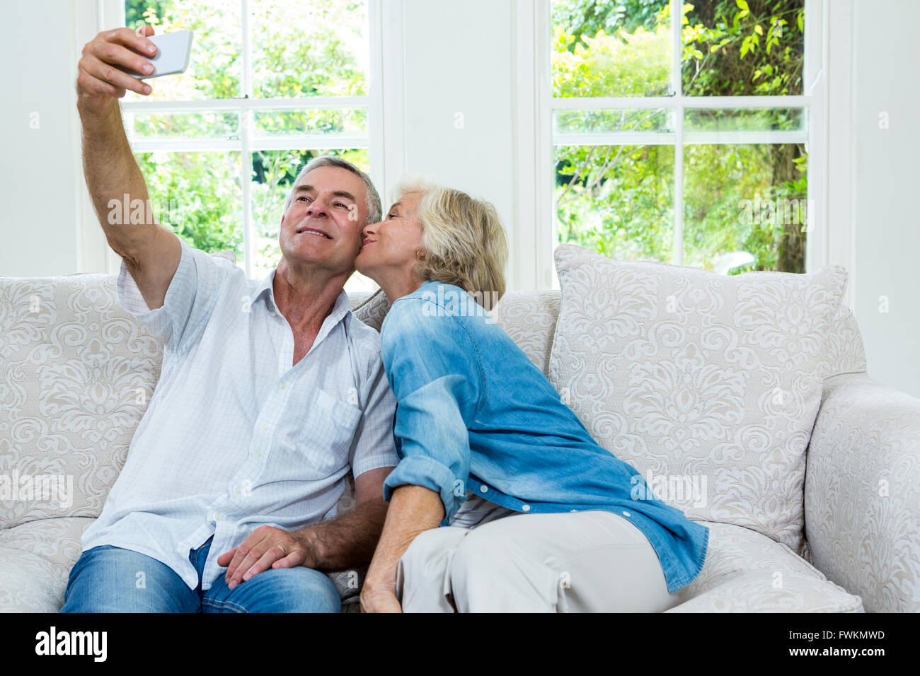 Senior donna baciare mentre l uomo prendendo selfie in salotto Foto Stock
