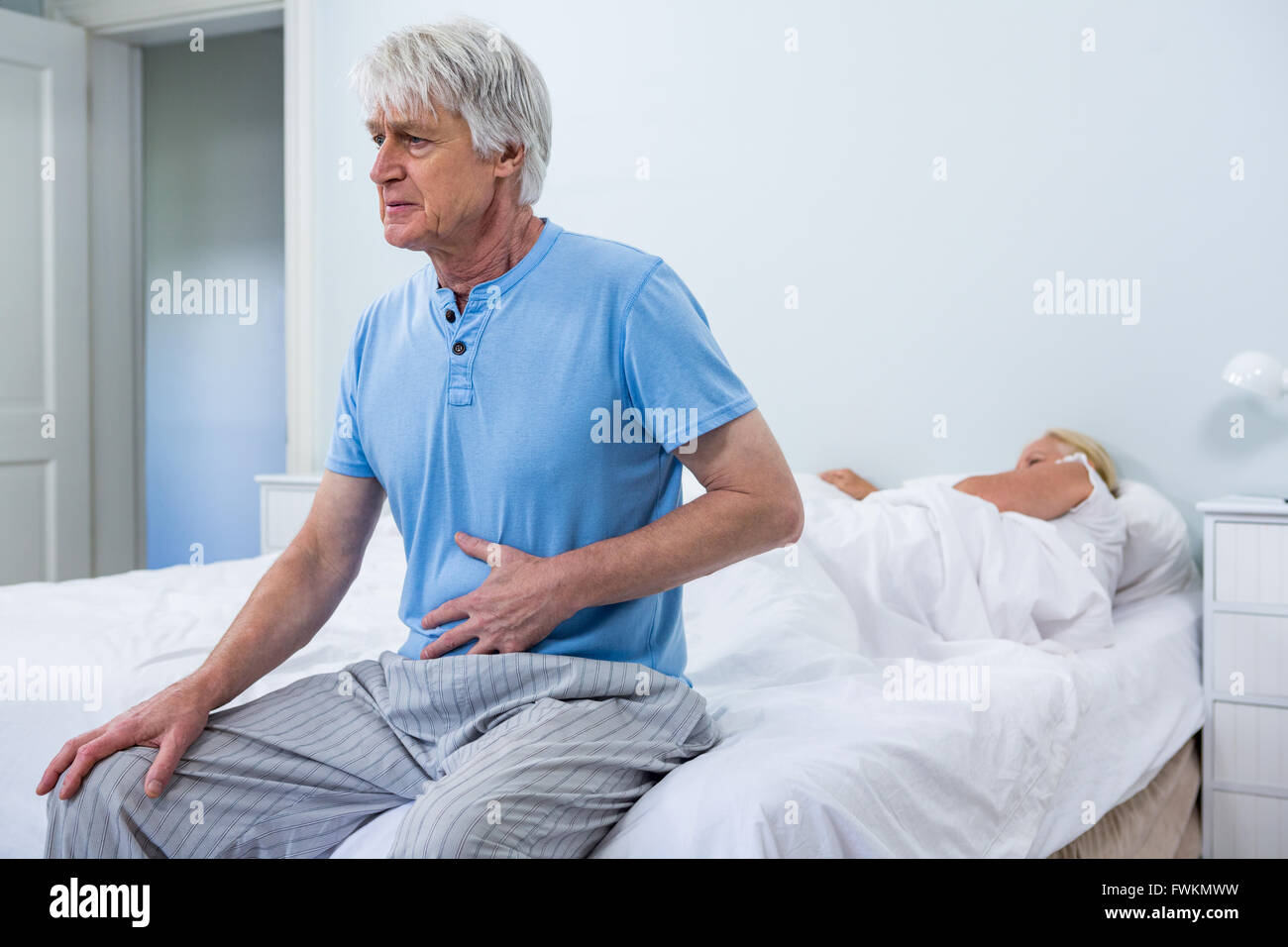 Senior man aventi dolore allo stomaco mentre è seduto sul letto Foto Stock
