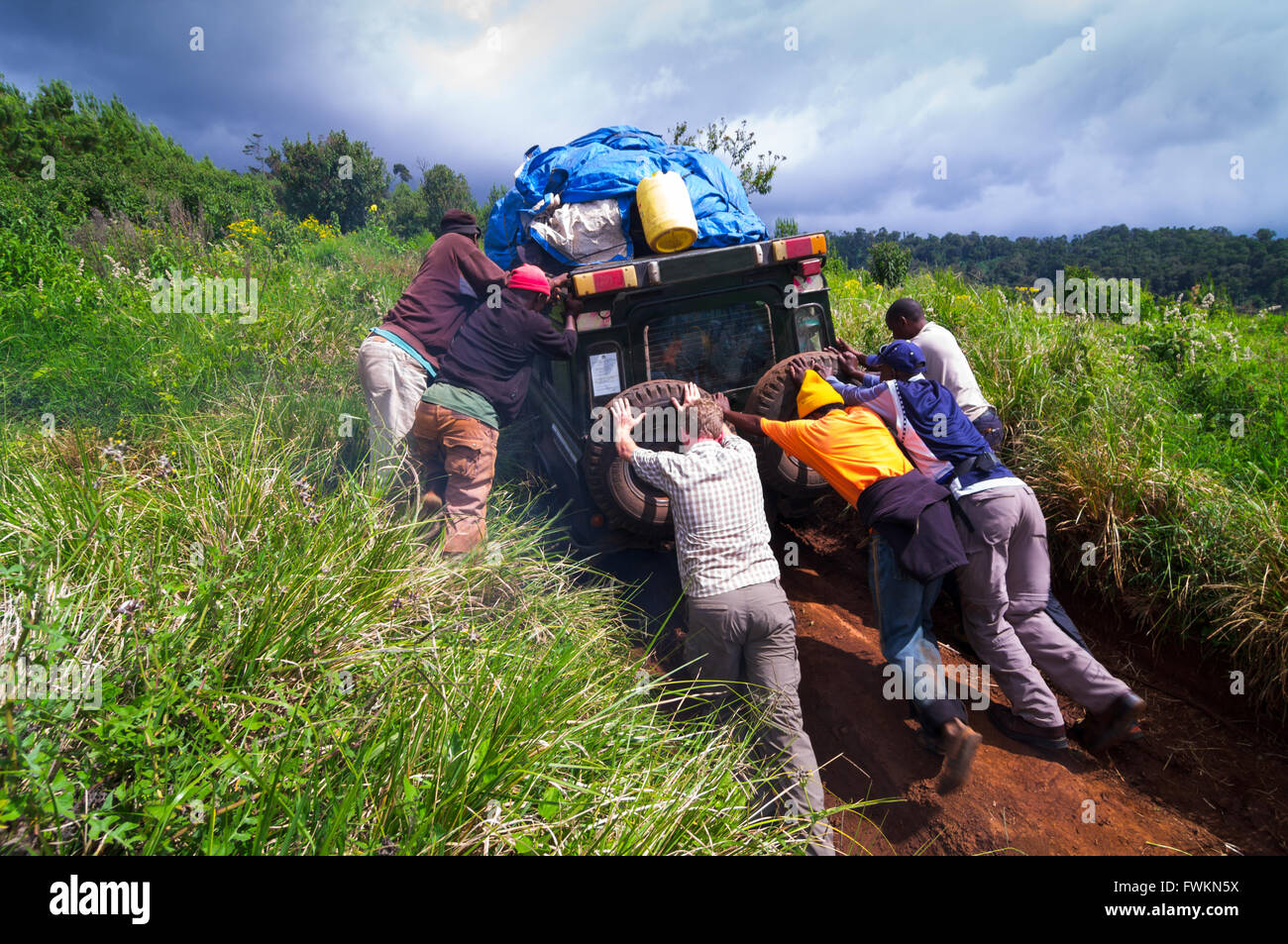 Gli uomini cercano di spingere il veicolo 4WD fino e ripida strada sdrucciolevole all inizio del percorso Lemosho, Mt Kilimanjaro, Tanzania Africa Foto Stock