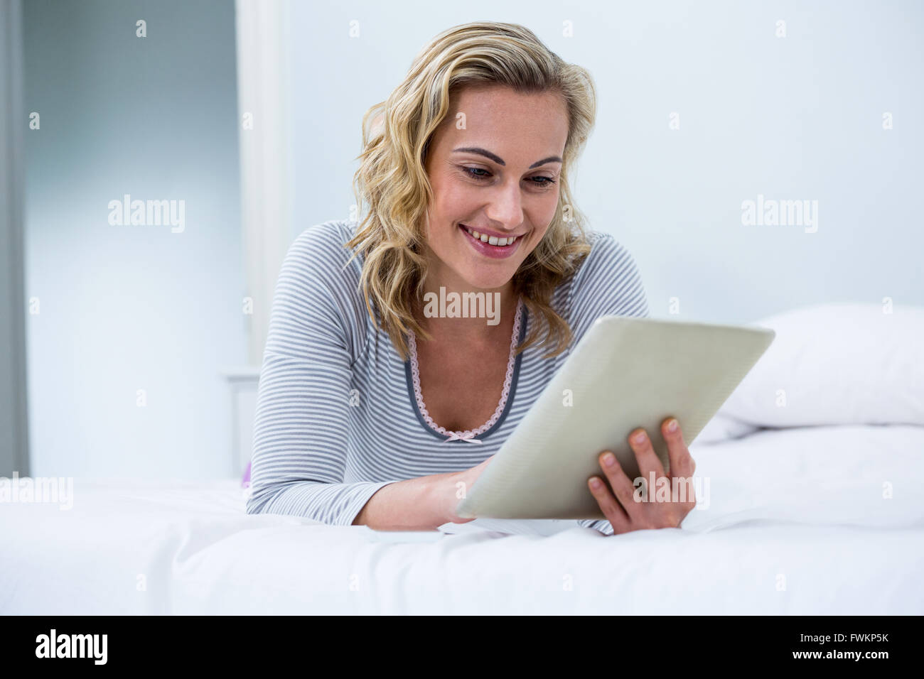 Giovane donna con tavoletta digitale sul letto Foto Stock