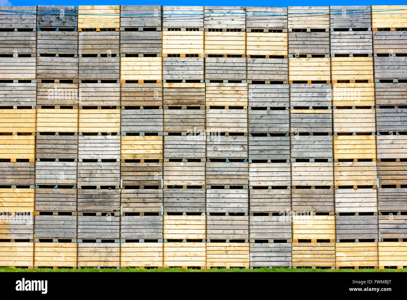 Un sacco di cassette di legno su pallet impilati come una parete alta. Scheggia di cielo blu in alto. Foto Stock