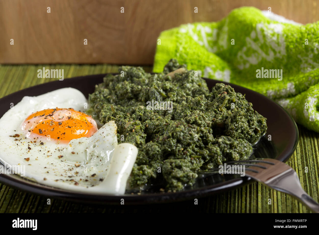 Stufati di ortiche con aglio e un uovo sulla piastra scuro con forca Foto Stock