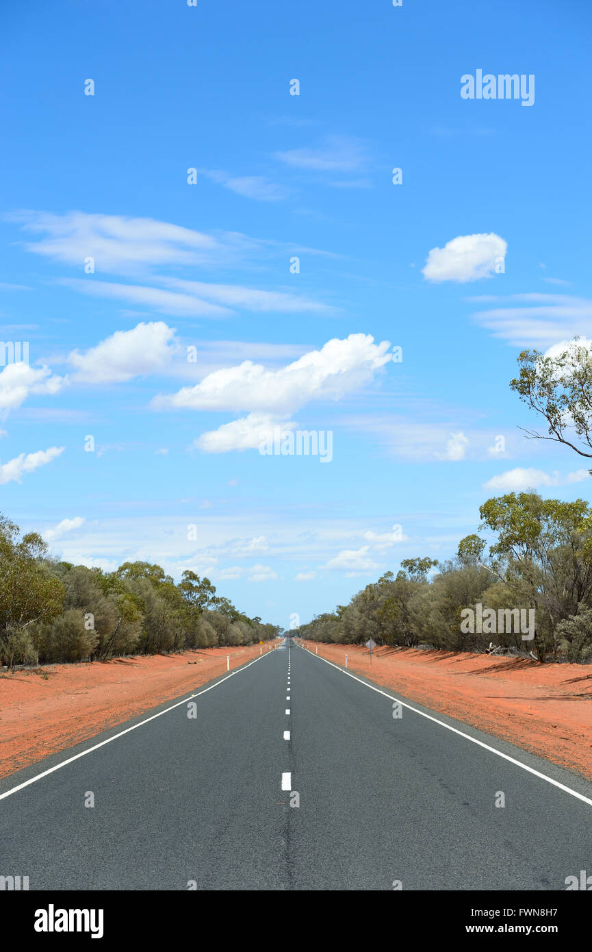 Outback australiano a due corsie con terra rossa, macchia verde e blu cielo cloud. Foto di Chris Ison. Foto Stock