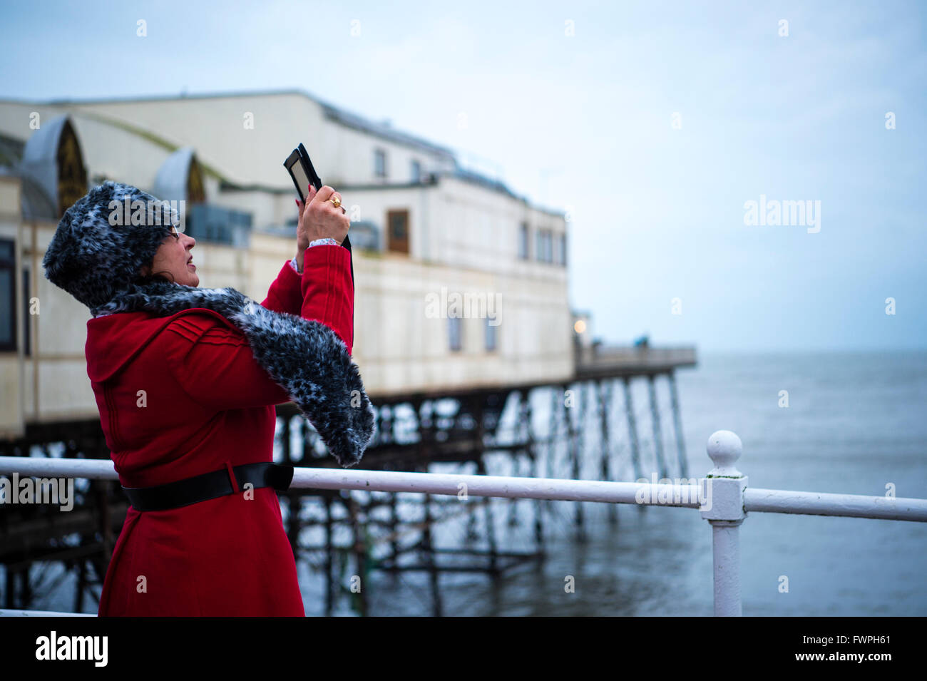 Una donna su Aberystwyth promenade di filmare i branchi di storni in quanto essi formano un murmuration nel cielo sopra il molo prima sono ' appollaiati per la notte Foto Stock