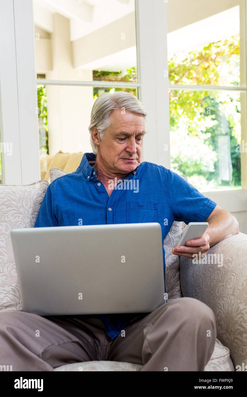 Senior uomo utilizzando il telefono cellulare mentre si lavora sul computer portatile Foto Stock