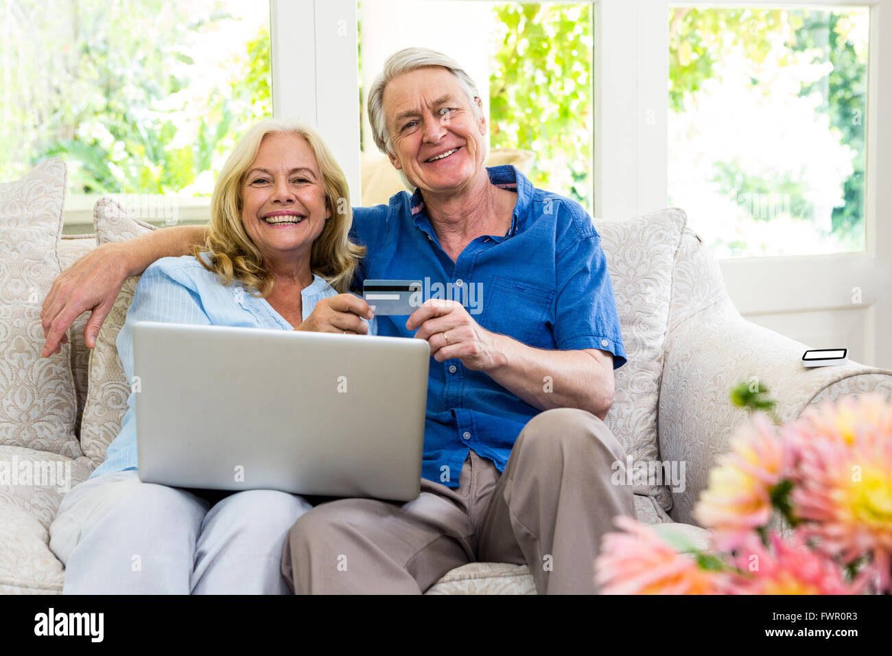 Felice coppia senior azienda smart card con il computer portatile mentre è seduto a casa Foto Stock