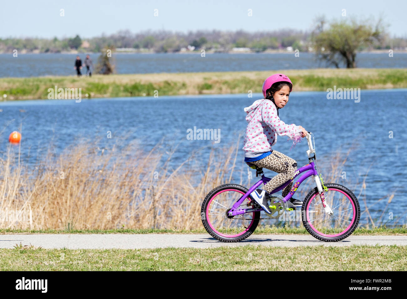 Una piccola ragazza ispanica cavalca la sua bicicletta per esercitare sul lago Overholser sentieri nella città di Oklahoma, Oklahoma, Stati Uniti d'America. Foto Stock