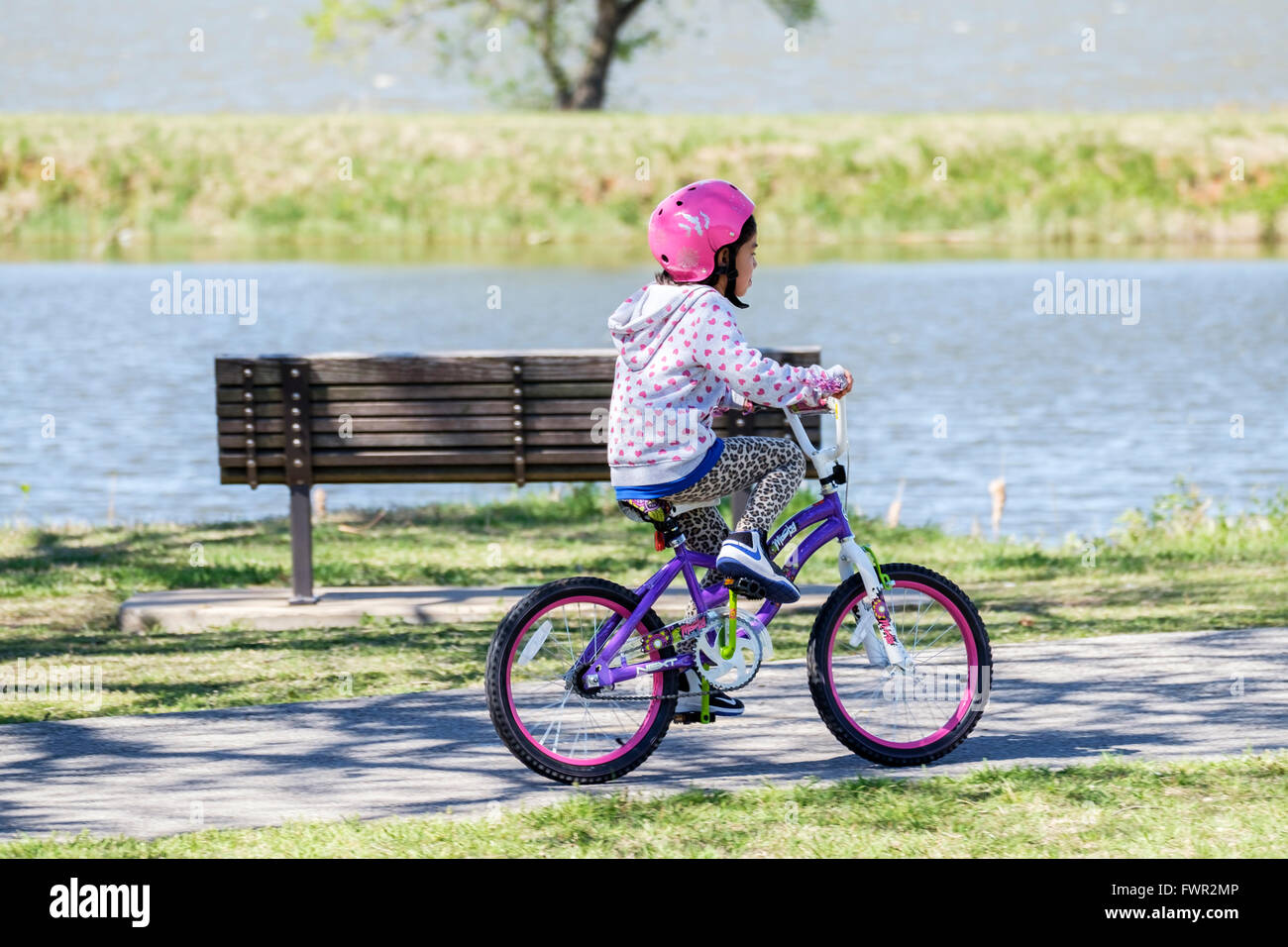 Una piccola ragazza ispanica cavalca la sua bicicletta per esercitare sul lago Overholser sentieri nella città di Oklahoma, Oklahoma, Stati Uniti d'America. Foto Stock