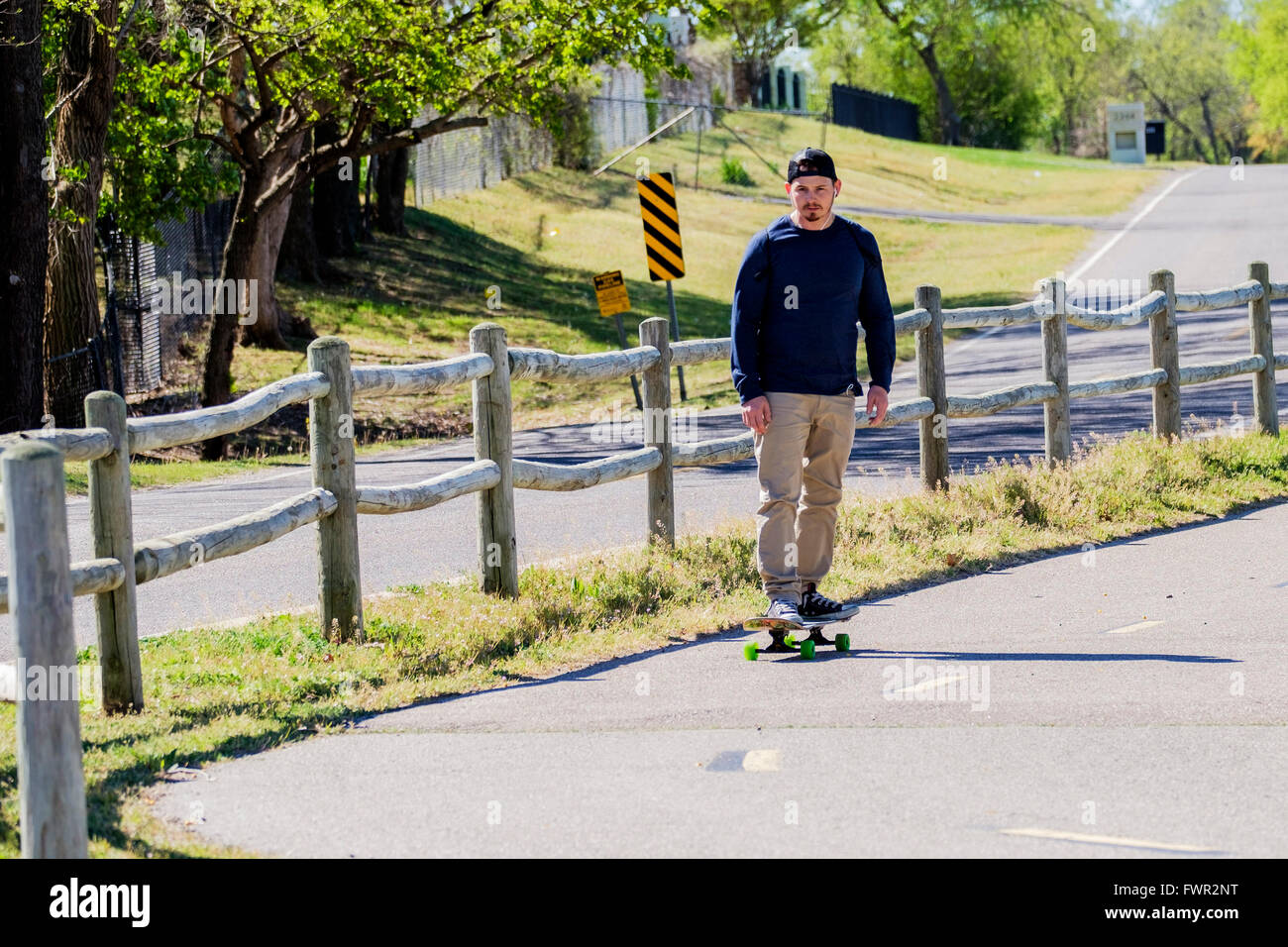 Un giovane uomo caucasico nella sua 20s di skateboard sul lago Overholser sentieri nella città di Oklahoma, Oklahoma, Stati Uniti d'America. Foto Stock