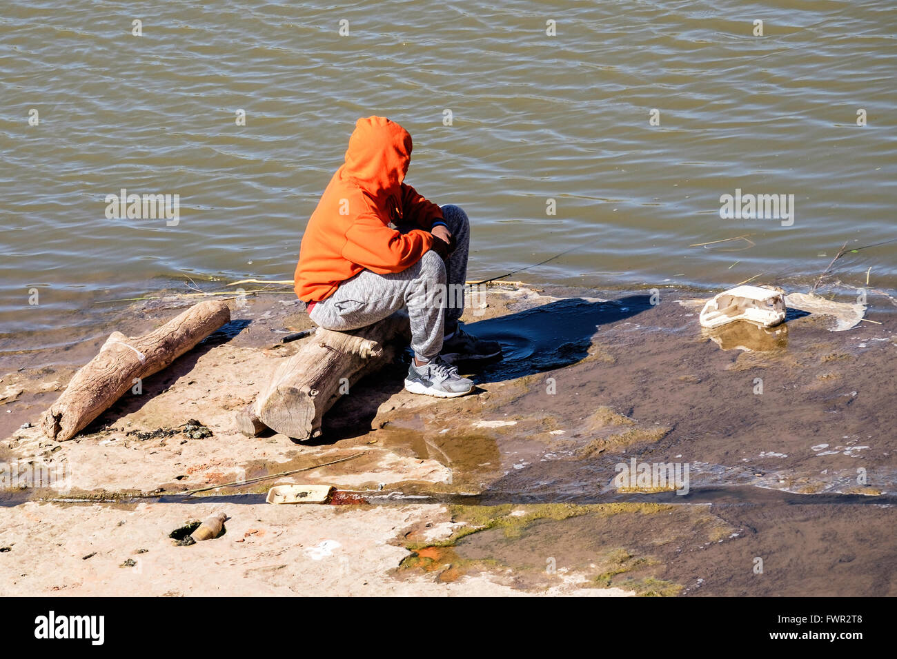 Un uomo in un hoodie siede su un registro e i pesci nel nord del fiume canadese in Oklahoma,USA.. Foto Stock