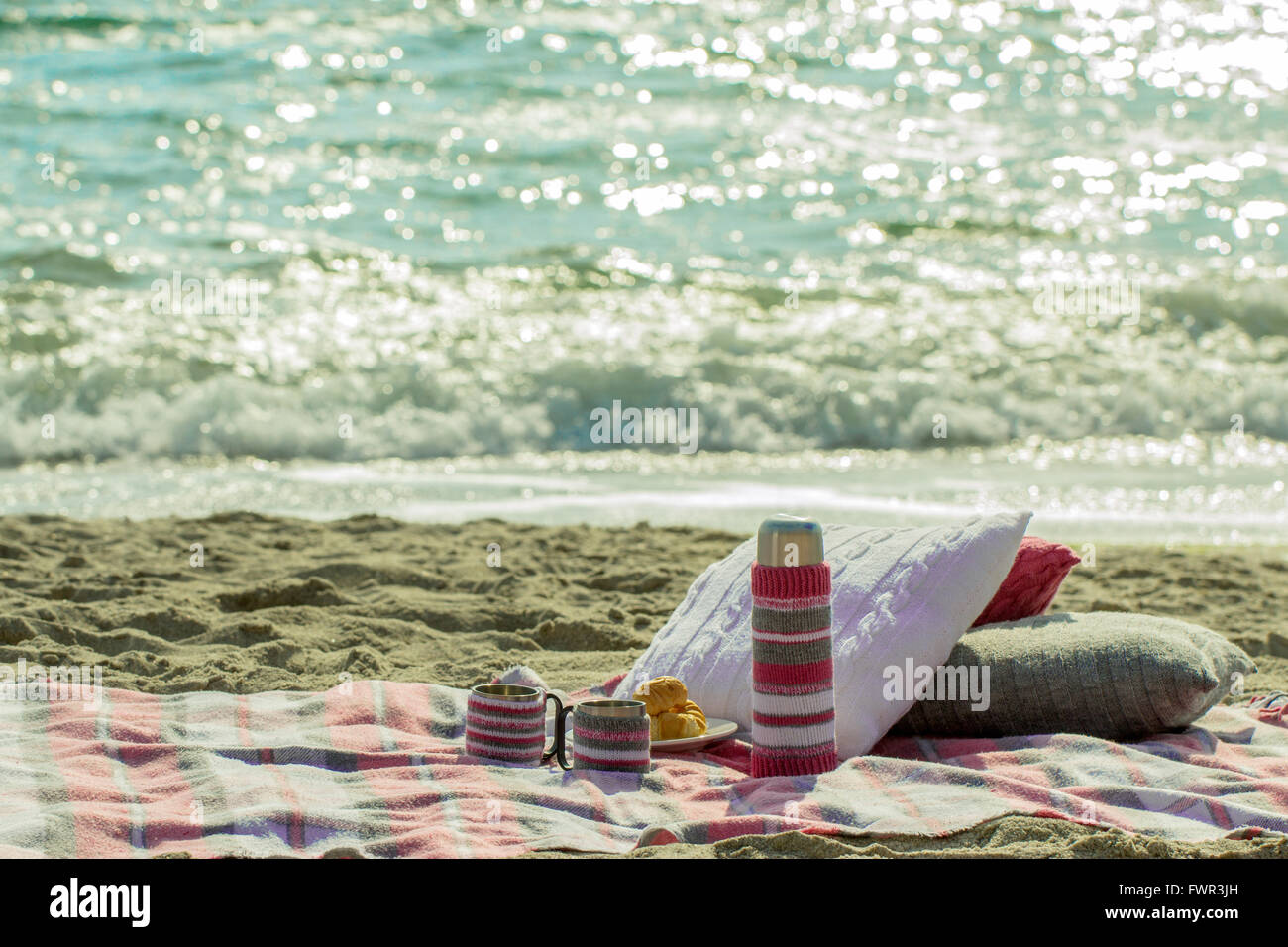 La prima colazione sulla spiaggia. Caffè e Croissant sul mare. Cuscini, custodia un thermos e Cup - per maglieria a mano. Foto Stock