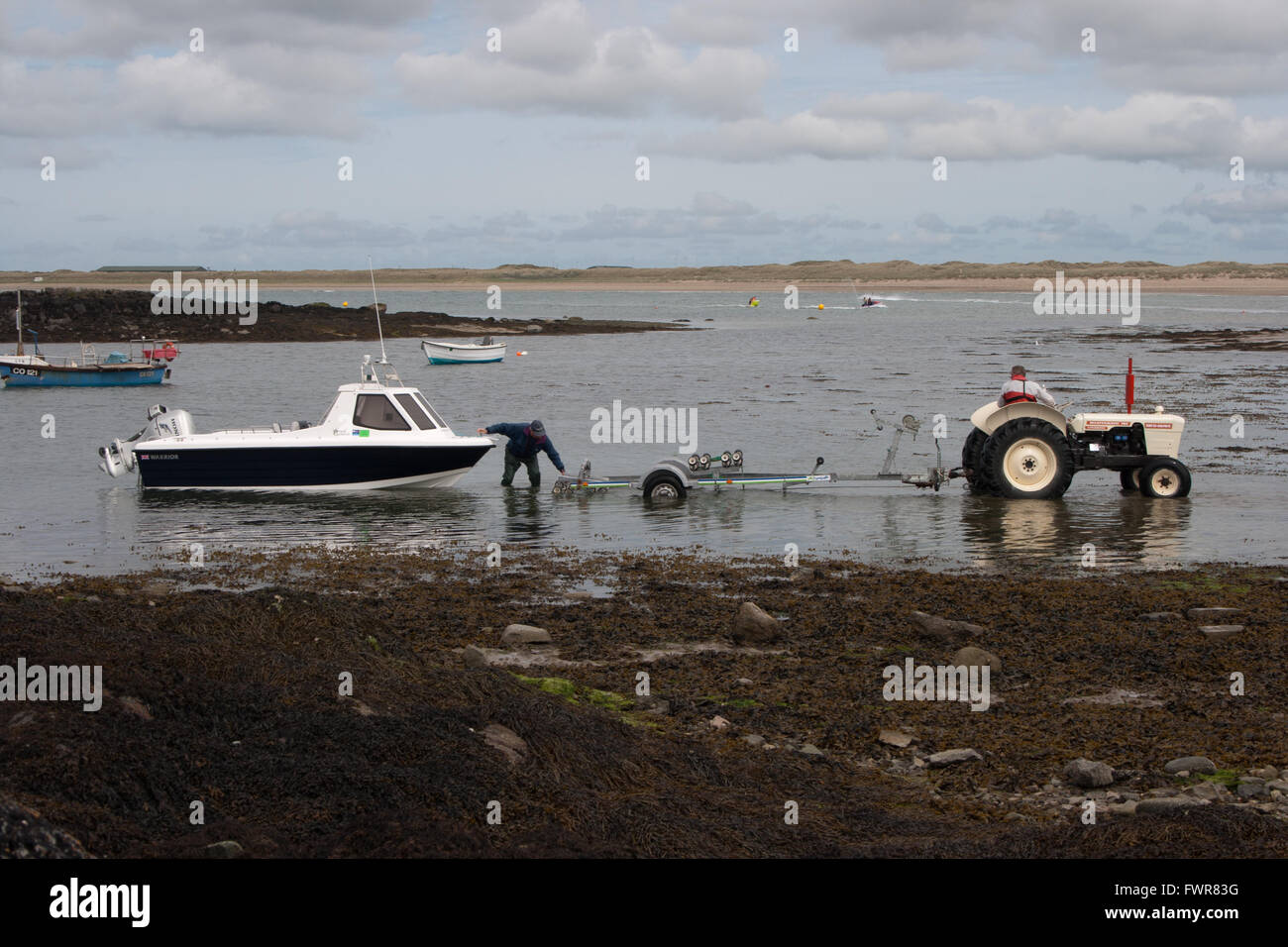 Due uomini preparare una piccola barca da pesca di essere presi al di fuori del mare su un carrello di lancio trainato da un bianco trattori David Brown. Foto Stock