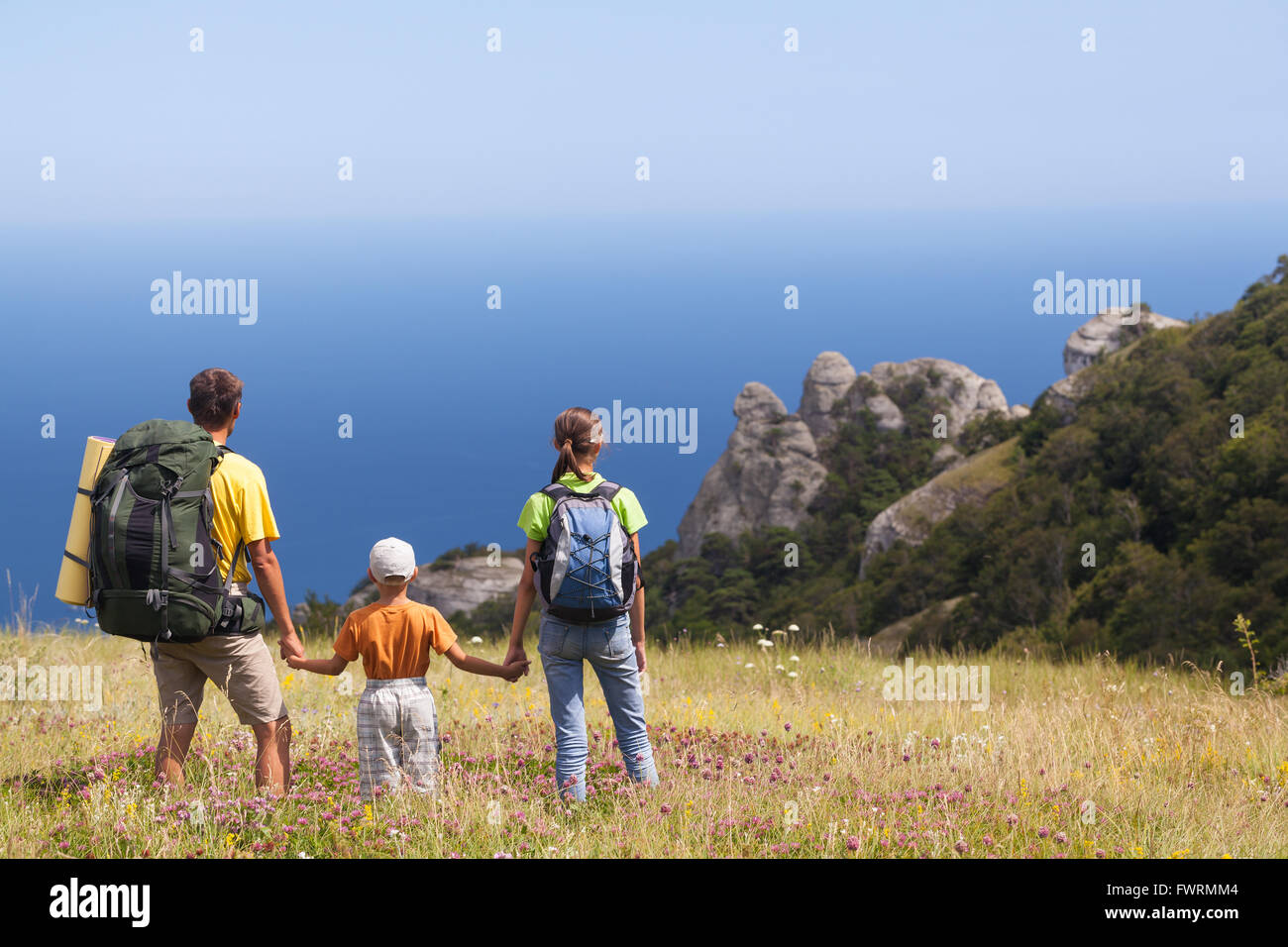 Famiglia a piedi con gli zaini sul campo e guardando la horizont al di sopra di mare Foto Stock