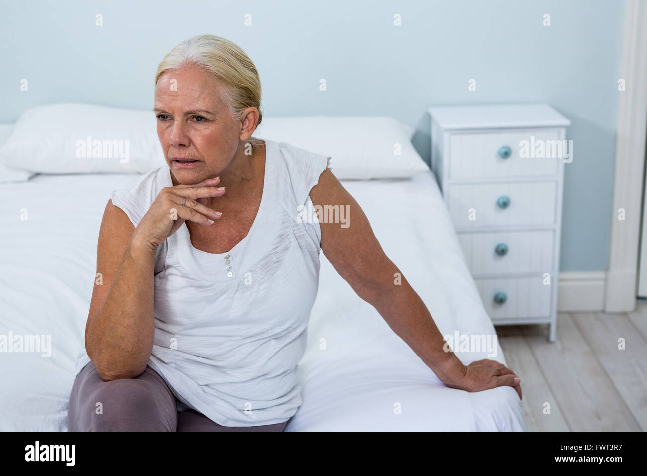 Sconvolto senior donna seduta sul letto in camera da letto Foto Stock