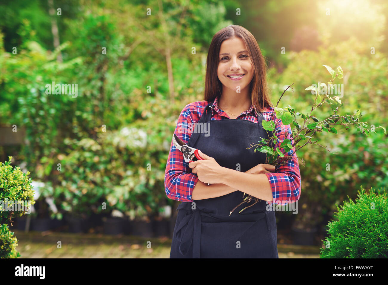 Felice fiducioso attraente giovane donna la potatura di piante in vivaio come essa celebra il suo successo come un imprenditore con la sua propria Foto Stock