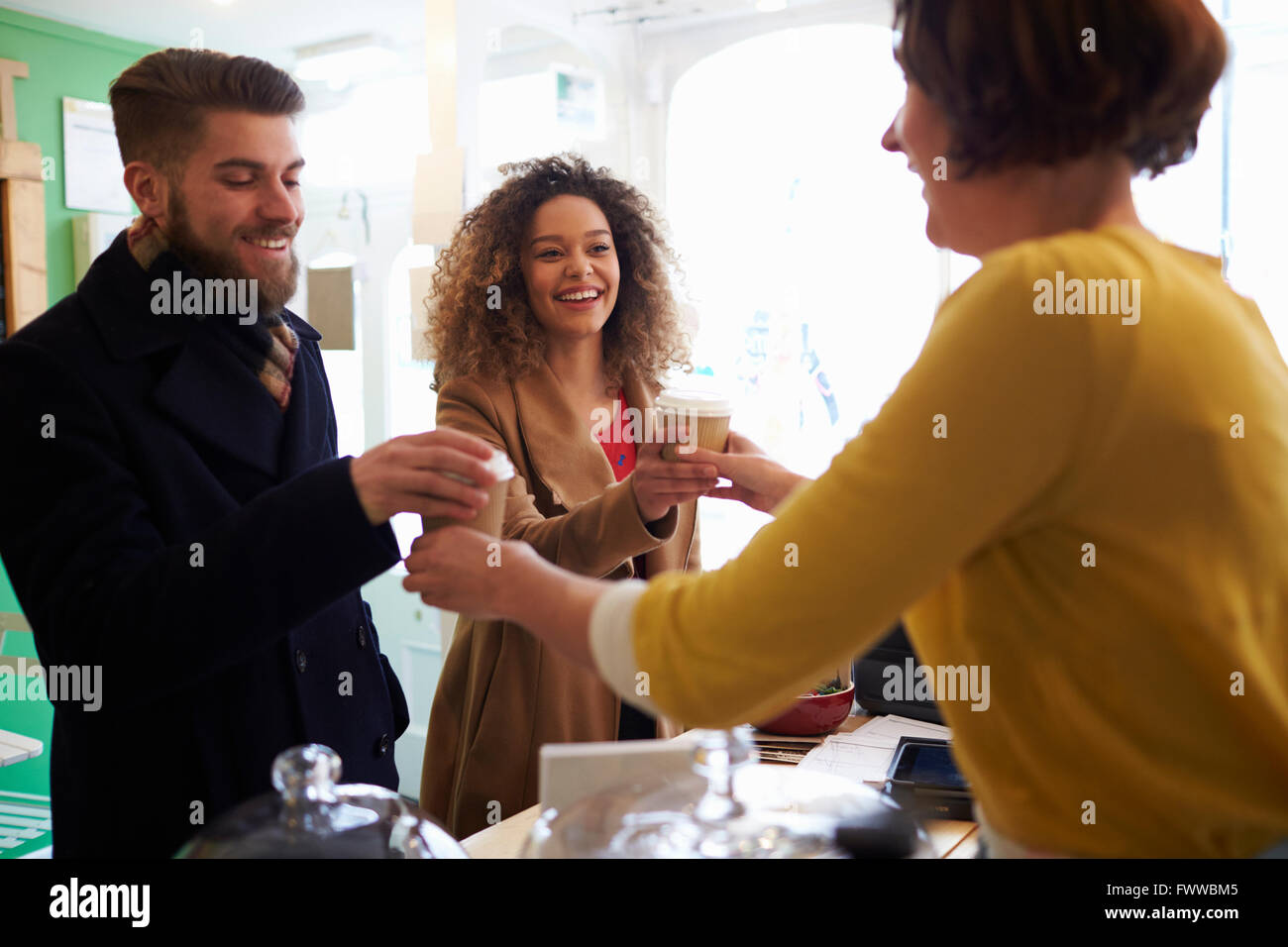 Il proprietario di un coffee shop che serve giovane con bevande da asporto Foto Stock