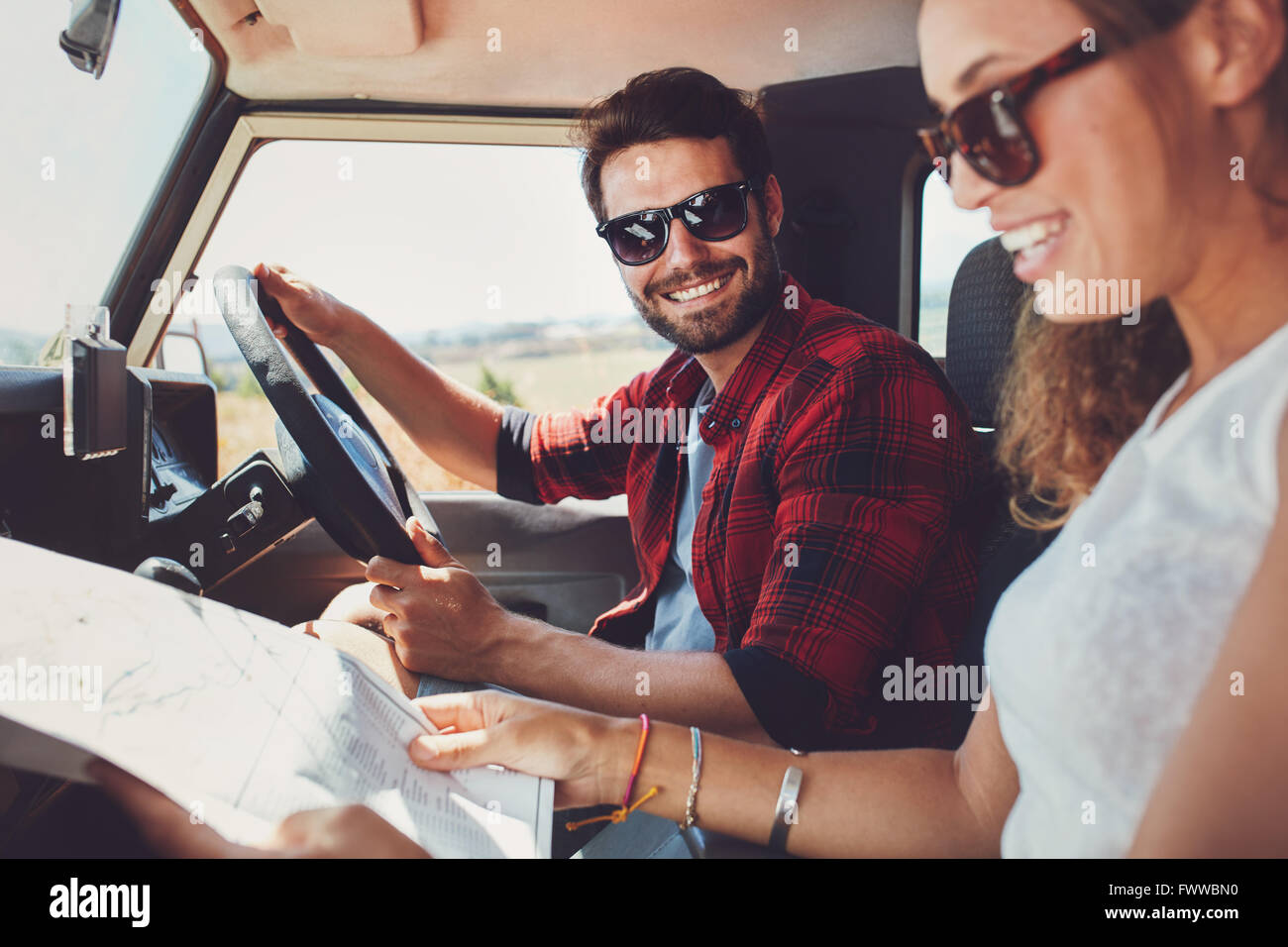 Coppia giovane seduto dentro la loro auto con mappa. Sorridente giovane uomo e donna seduta insieme e guardando la mappa per directio Foto Stock