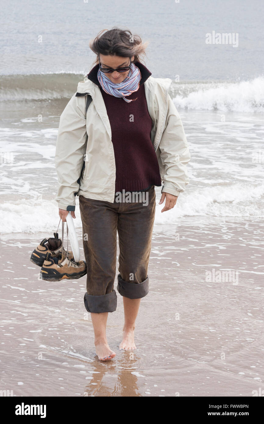 Donna che mantiene le scarpe e Frisbee paddling in mare. Regno Unito Foto Stock