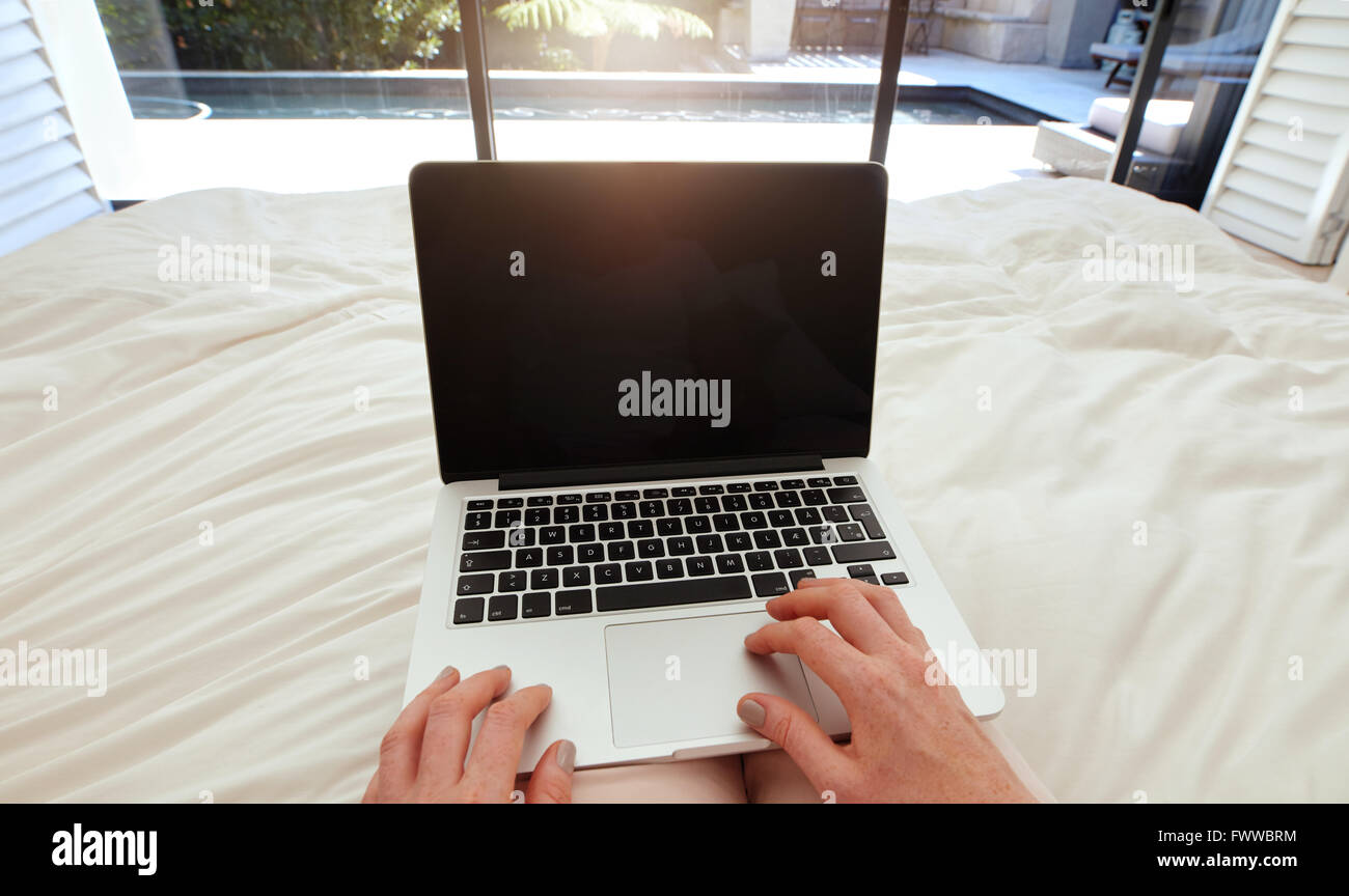 Primo piano immagine della donna su un letto lavorando sul computer portatile. POV shot di donna rilassante nella camera da letto utilizzando laptop. Foto Stock