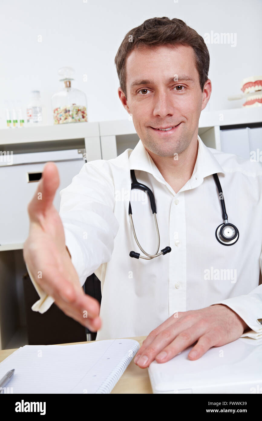 Medico al suo banco offrendo la mano per stretta di mano nel suo ufficio Foto Stock