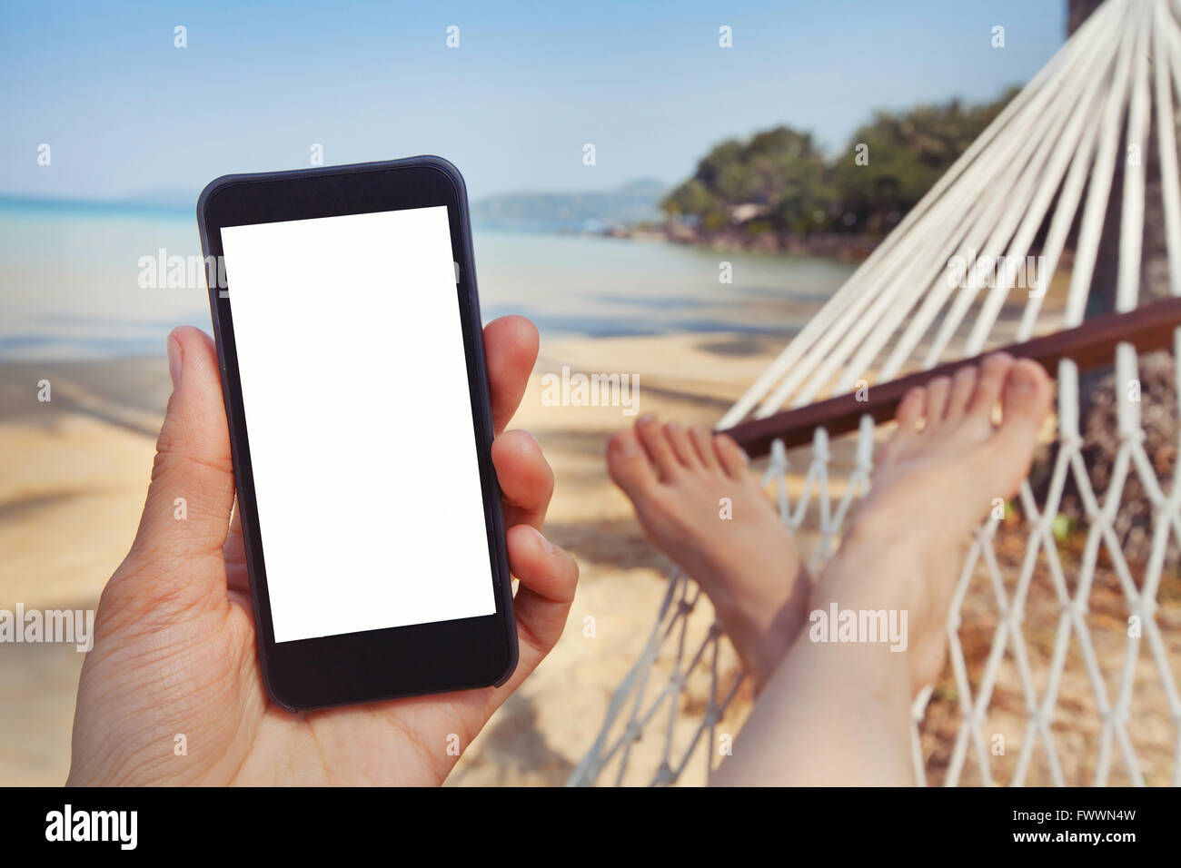 Applicazione mobile per viaggi, mano azienda smart phone con schermo bianco sulla spiaggia Foto Stock