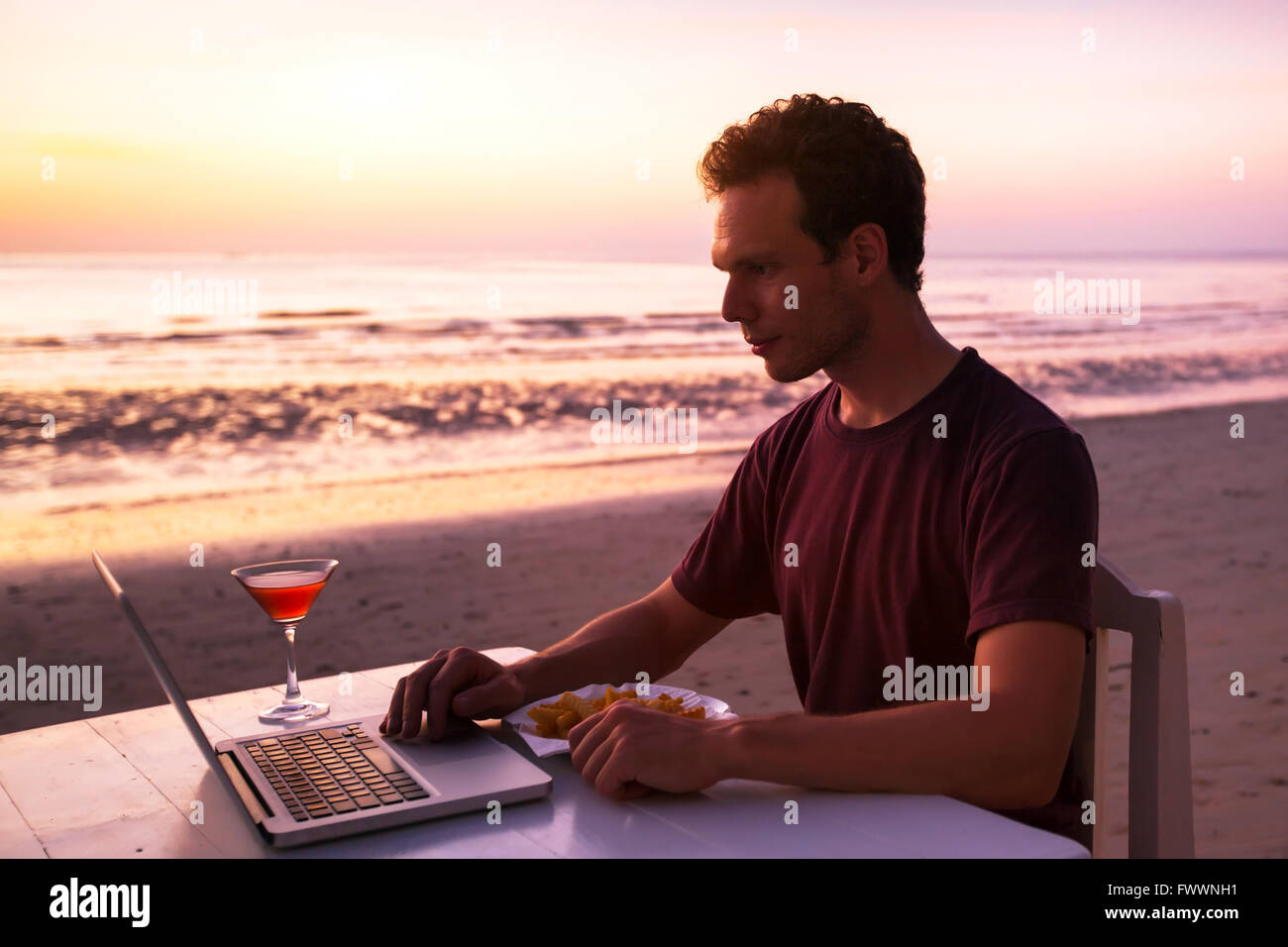 Uomo con notebook nel ristorante sulla spiaggia al tramonto Foto Stock