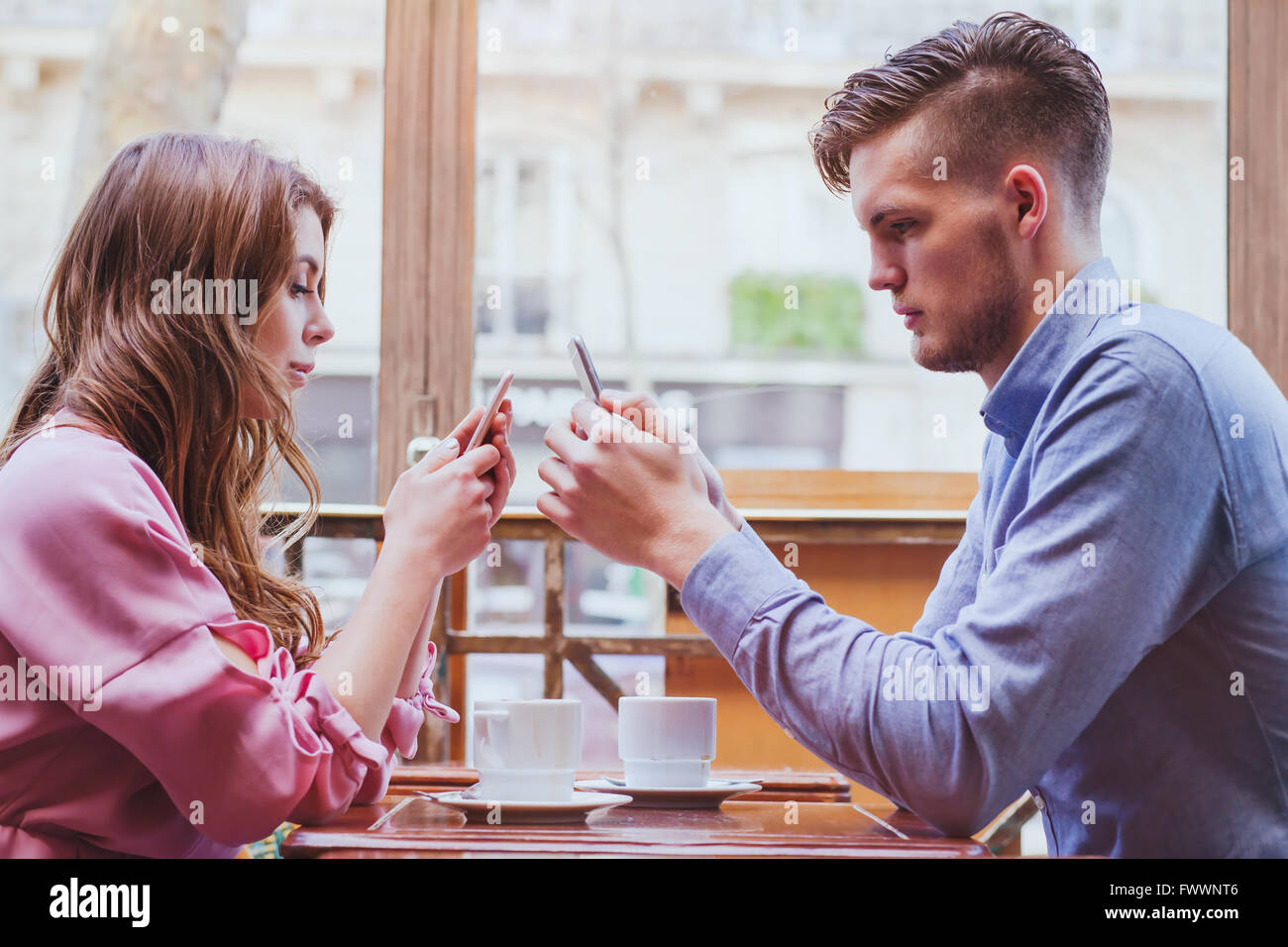 Sempre connessi e la dipendenza da internet, giovane coppia cafe guardando il loro smartphone, sociale un concetto di rete Foto Stock