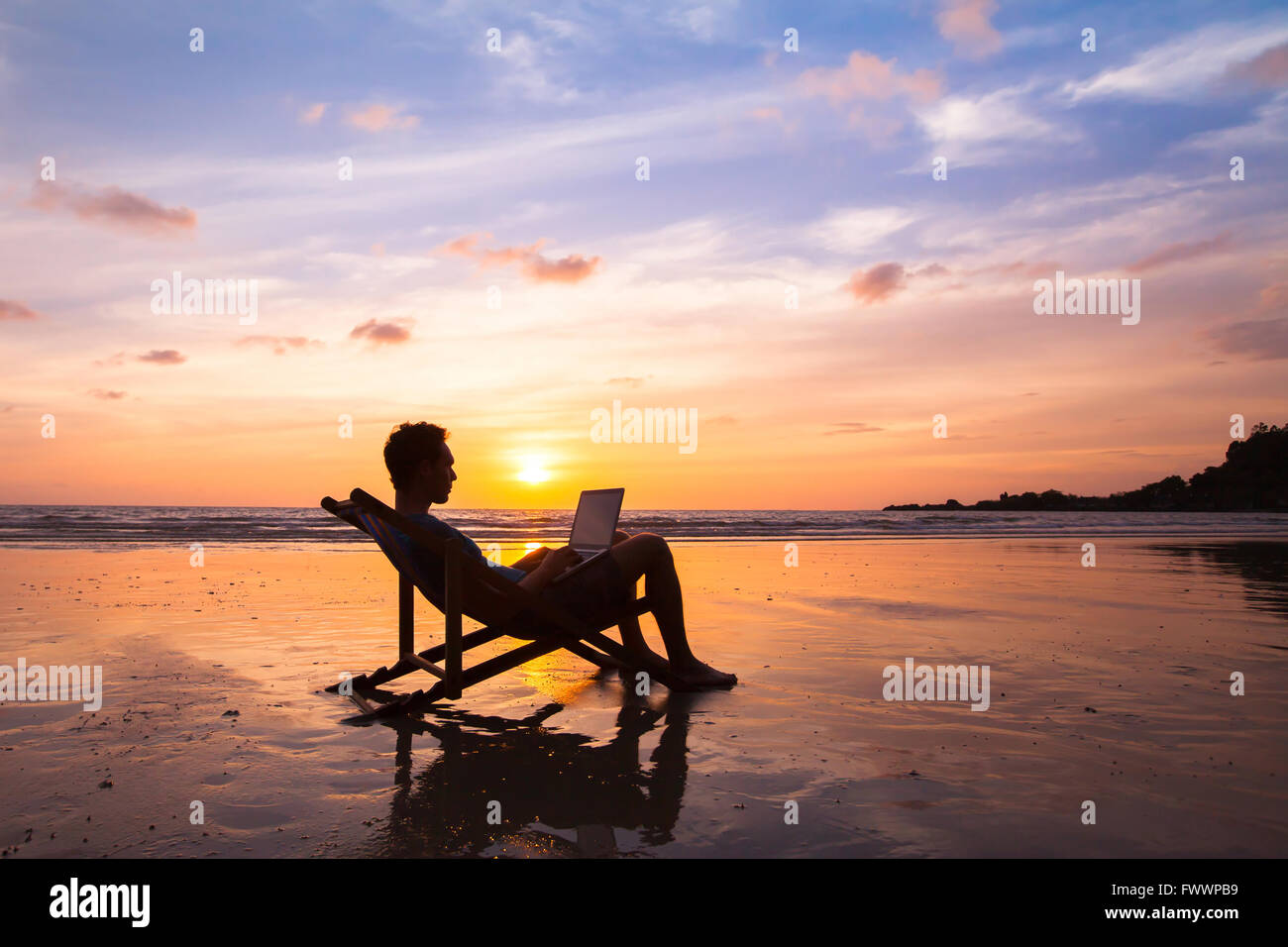 Silhouette di felice uomo d affari con computer portatile lavorando sulla spiaggia Foto Stock