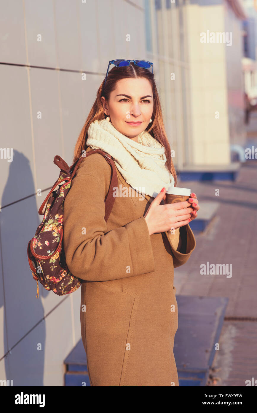 Bella bruna donna tenendo un sacco e tazza di tè o caffè caldo, in piedi in strada Foto Stock