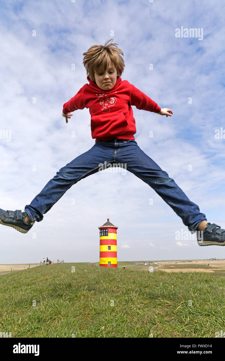 Ragazzo giovane jumping maggiore di Pilsum Lighthouse, East Friesland, Bassa Sassonia, Germania Foto Stock