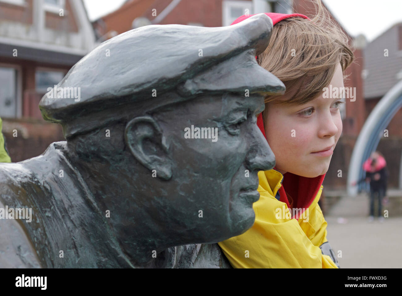 Giovane ragazzo accanto alla statua di un pescatore, porto di pescatori, Neuharlingersiel, East Friesland, Bassa Sassonia, Germania Foto Stock