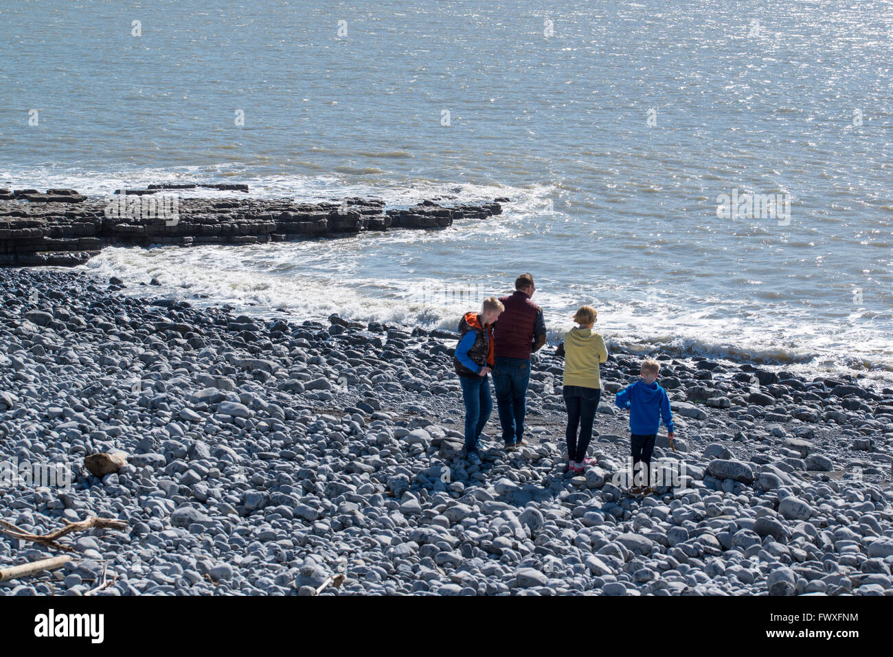 Una famiglia su di una spiaggia di ciottoli che guarda al mare. Foto Stock