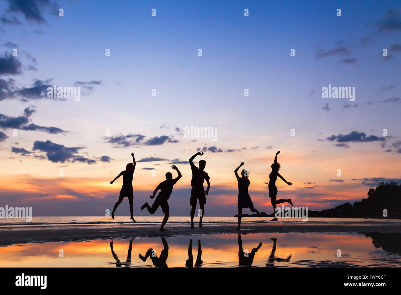 Gruppo di persone che saltano sulla spiaggia al tramonto, silhouette di amici divertendosi insieme Foto Stock