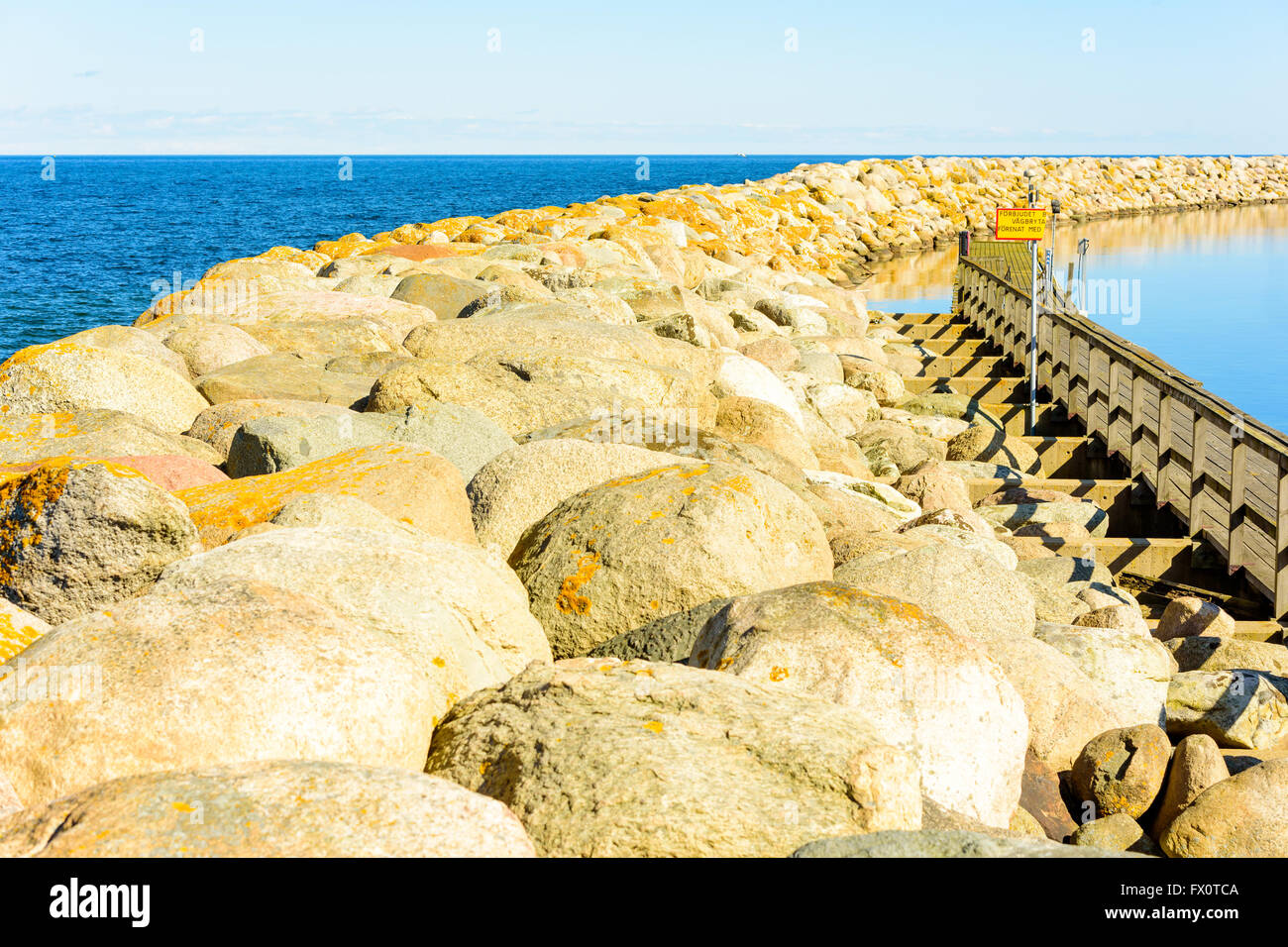 Piegatura molo di pietra su un windless giornata di primavera. Segno rotto mettere in guardia circa i pericoli sul molo in svedese. Foto Stock