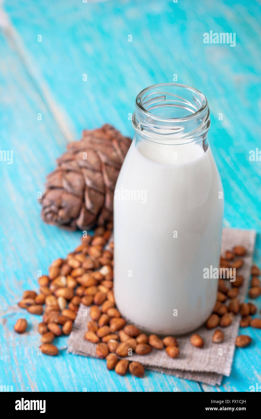 Il latte da i pinoli in una bottiglia di vetro, pinoli su un blu sullo sfondo di legno Foto Stock