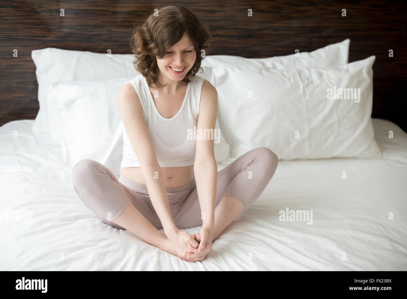 Gravidanza felice giovane donna facendo esercizio di yoga in camera da letto. Modello femminile di seduta sul letto in Baddha Konasana Foto Stock