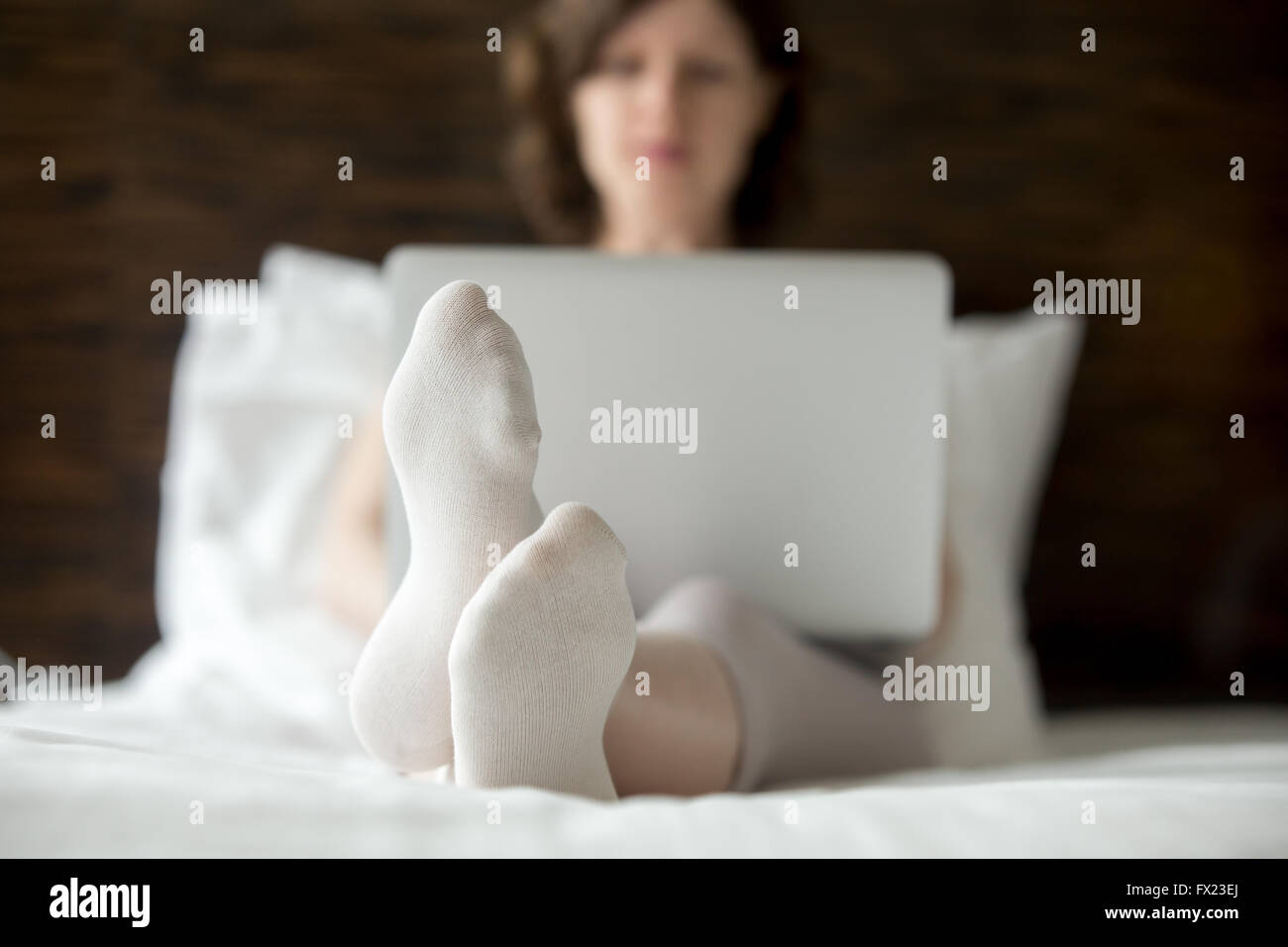 Bella giovane donna seduta sul letto tramite computer portatile in camera moderna. Modello caucasico rilassante con computer in ambienti interni Foto Stock