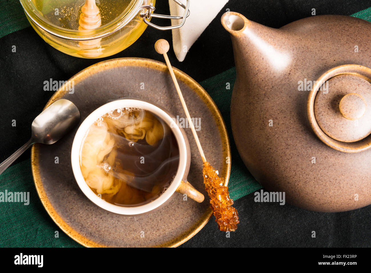 Una tazza di tè caldo su un tavolo con teiera e miele. Il latte è la miscelazione con tè Shot dal di sopra Foto Stock