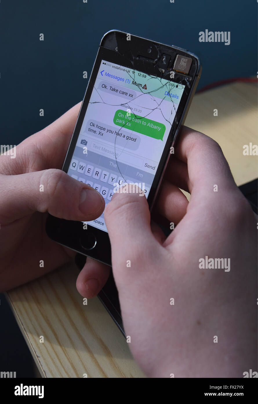 Ragazzo adolescente scrivere messaggi su un Apple iPhone 5s con uno schermo incrinato Foto Stock