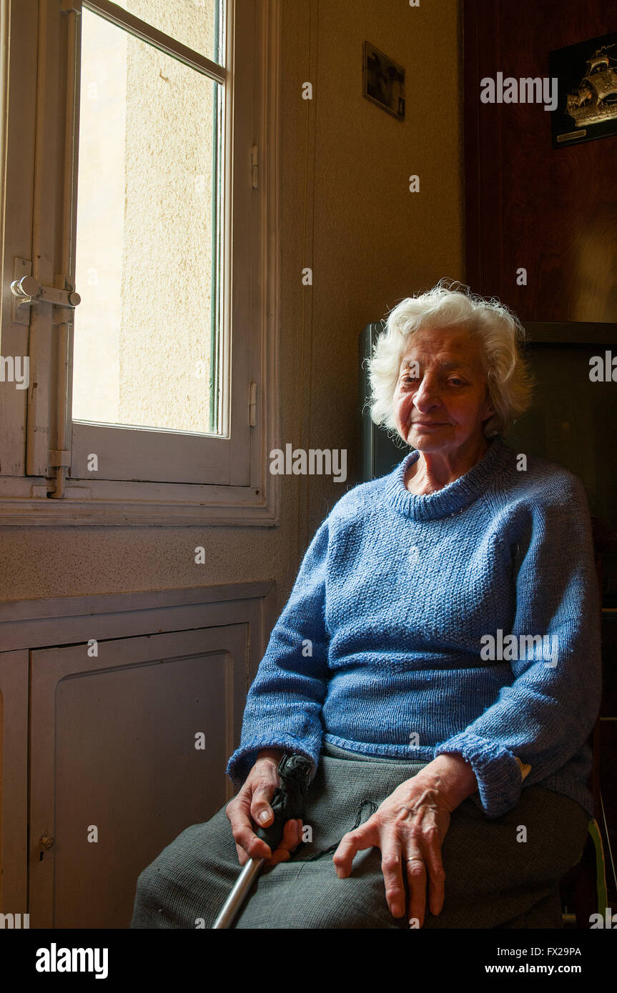 Vecchia donna in posa dalla finestra a casa sua. Foto Stock