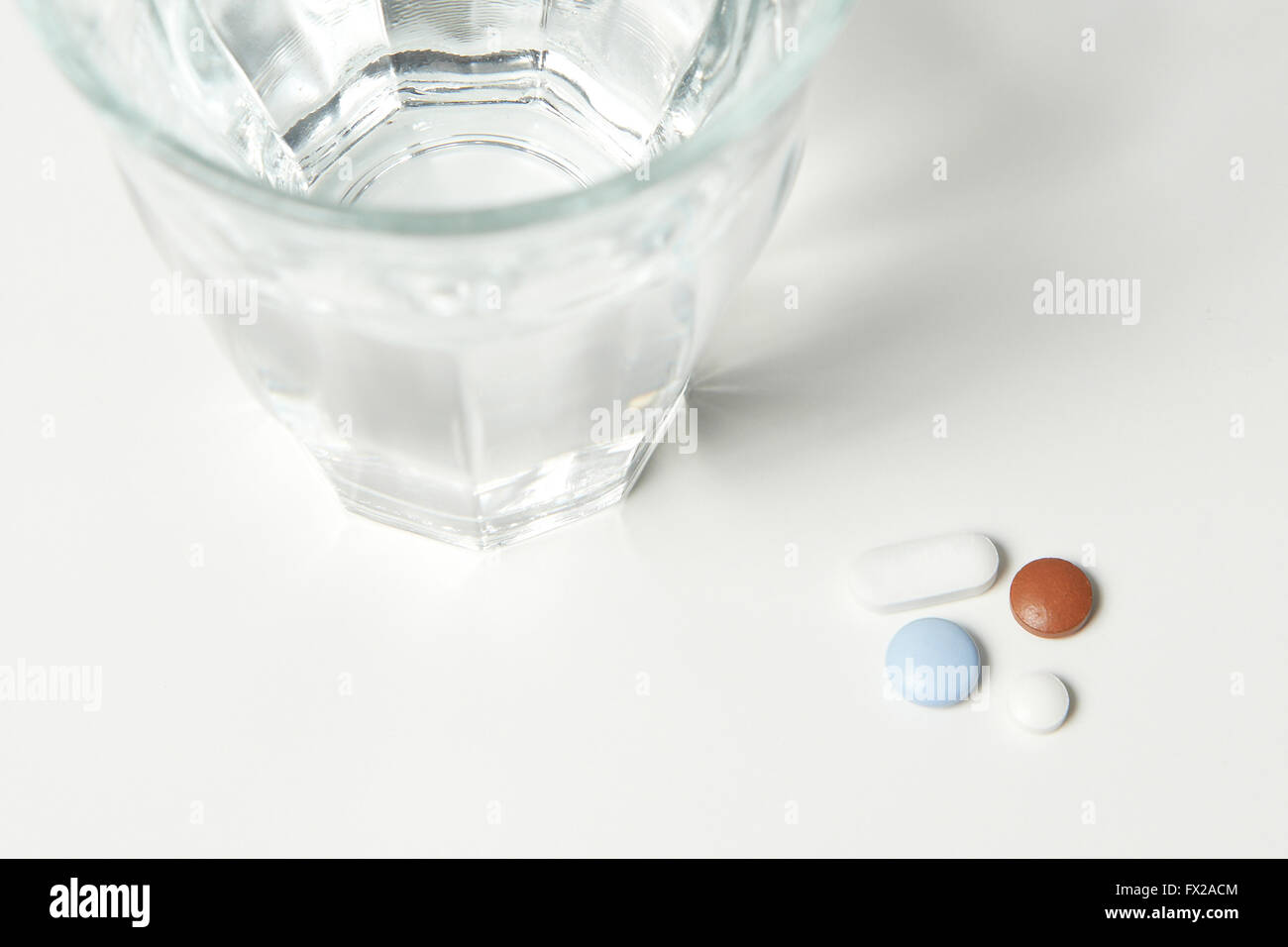 Pillole e un bicchiere di acqua su un tavolo bianco Foto Stock