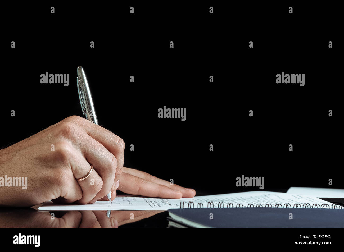 Stretta di mano umana firma sulla carta formale al tavolo. Sfondo nero. Foto Stock